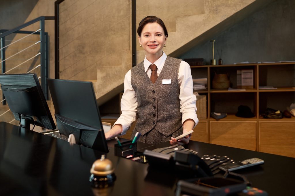 Introverte nachtreceptionist achter de hotelbalie in een stille lobby tijdens de nacht, met gedempt licht en een computer in gebruik